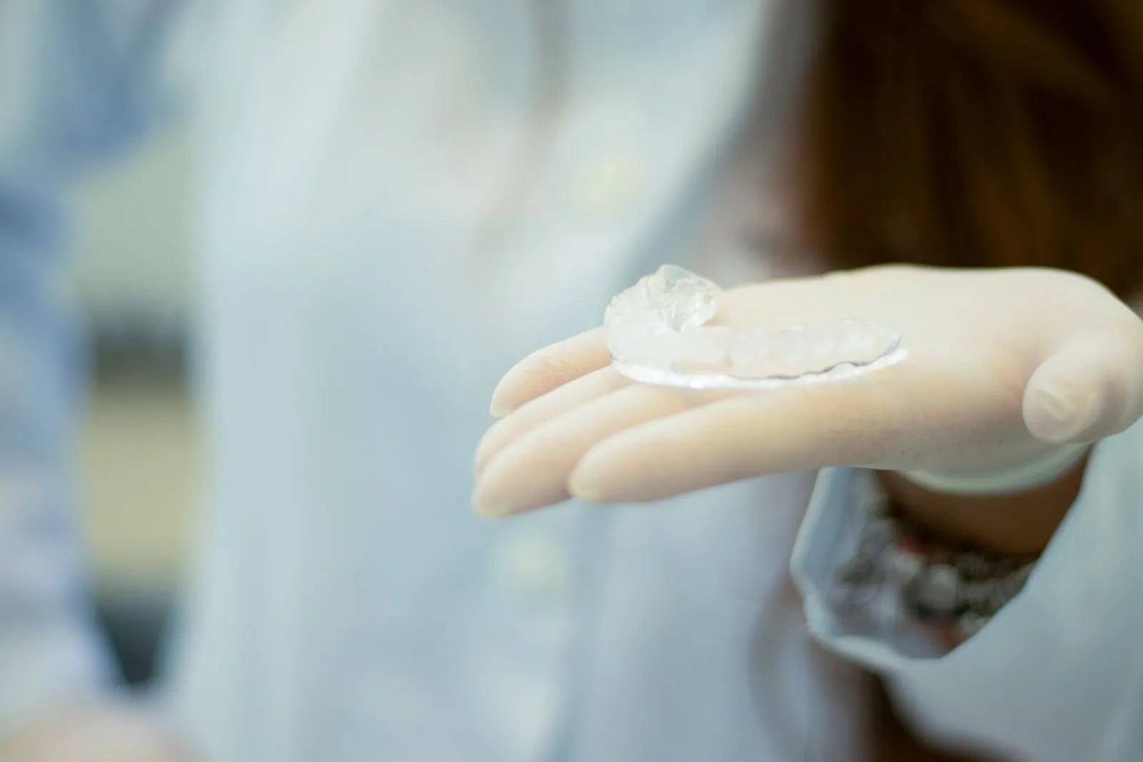 Gloved hand presenting a clear plastic mouth guard in a bright room
