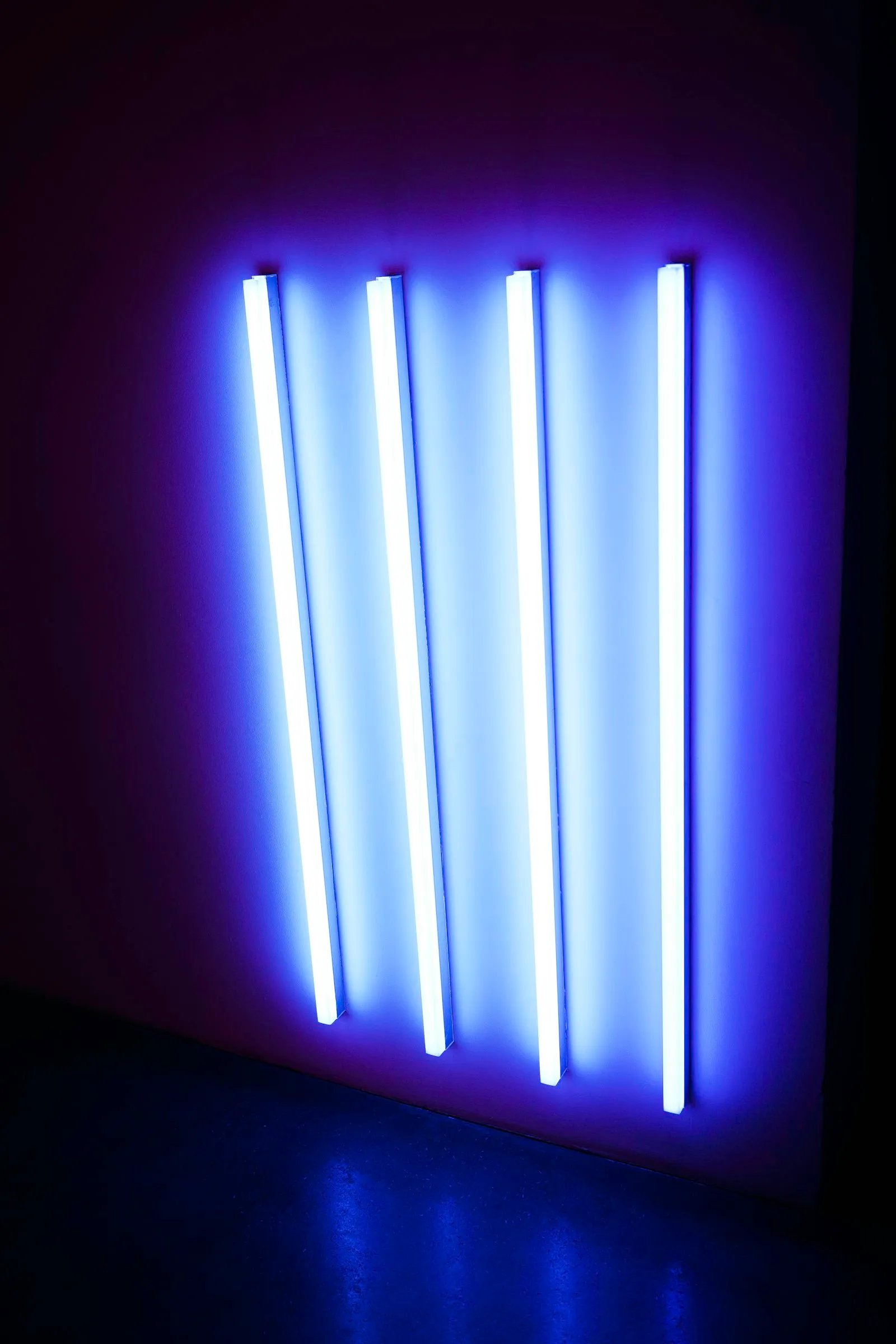 Four ultraviolet fluorescent tubes glowing blue and violet against a dark wall