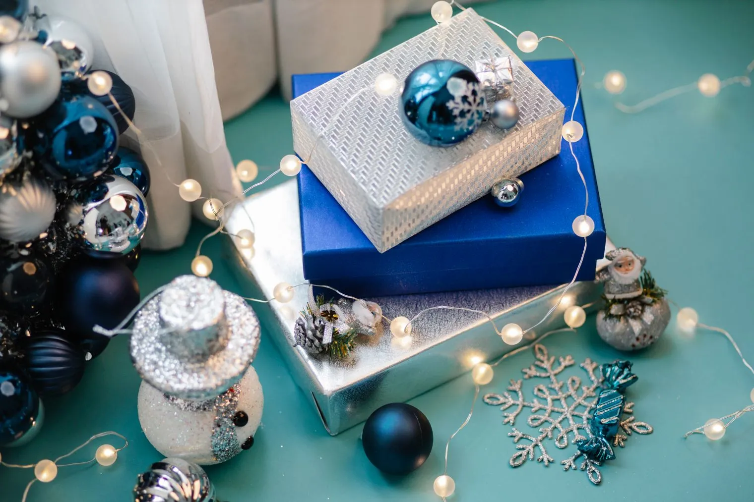 Wrapped gift boxes, blue baubles and fairy lights on a teal table