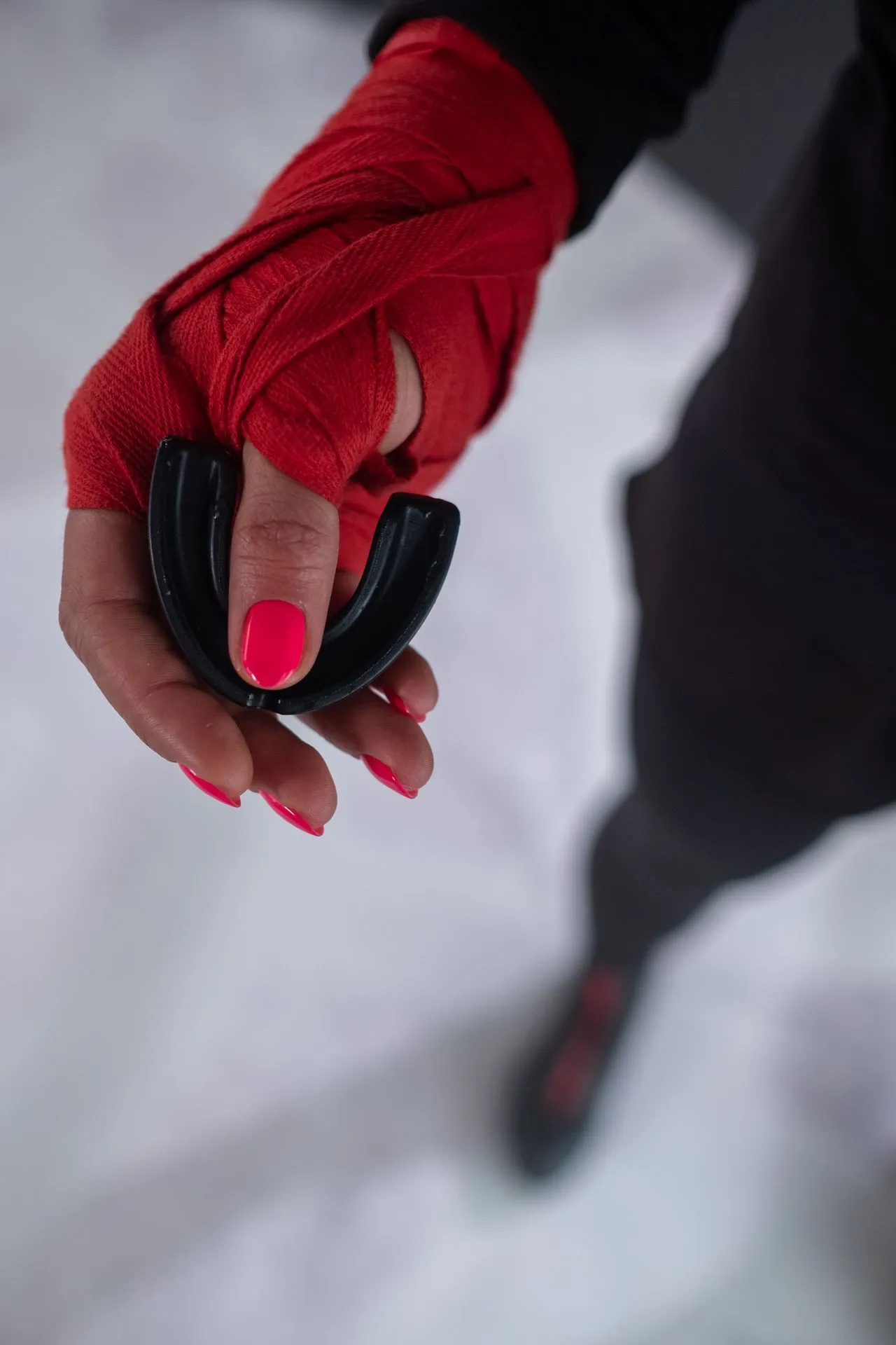 Hand in a red boxing wrap holding a black sports mouth guard