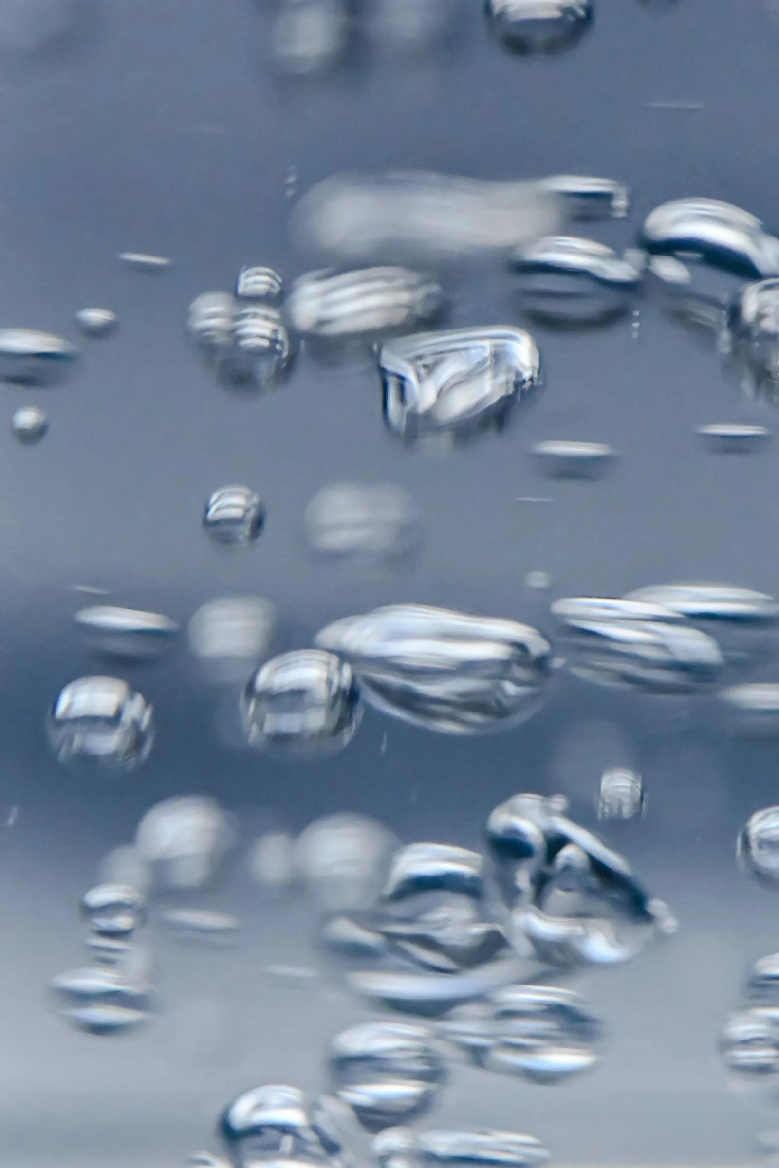Close-up of air bubbles rising through clear water against a blue ground